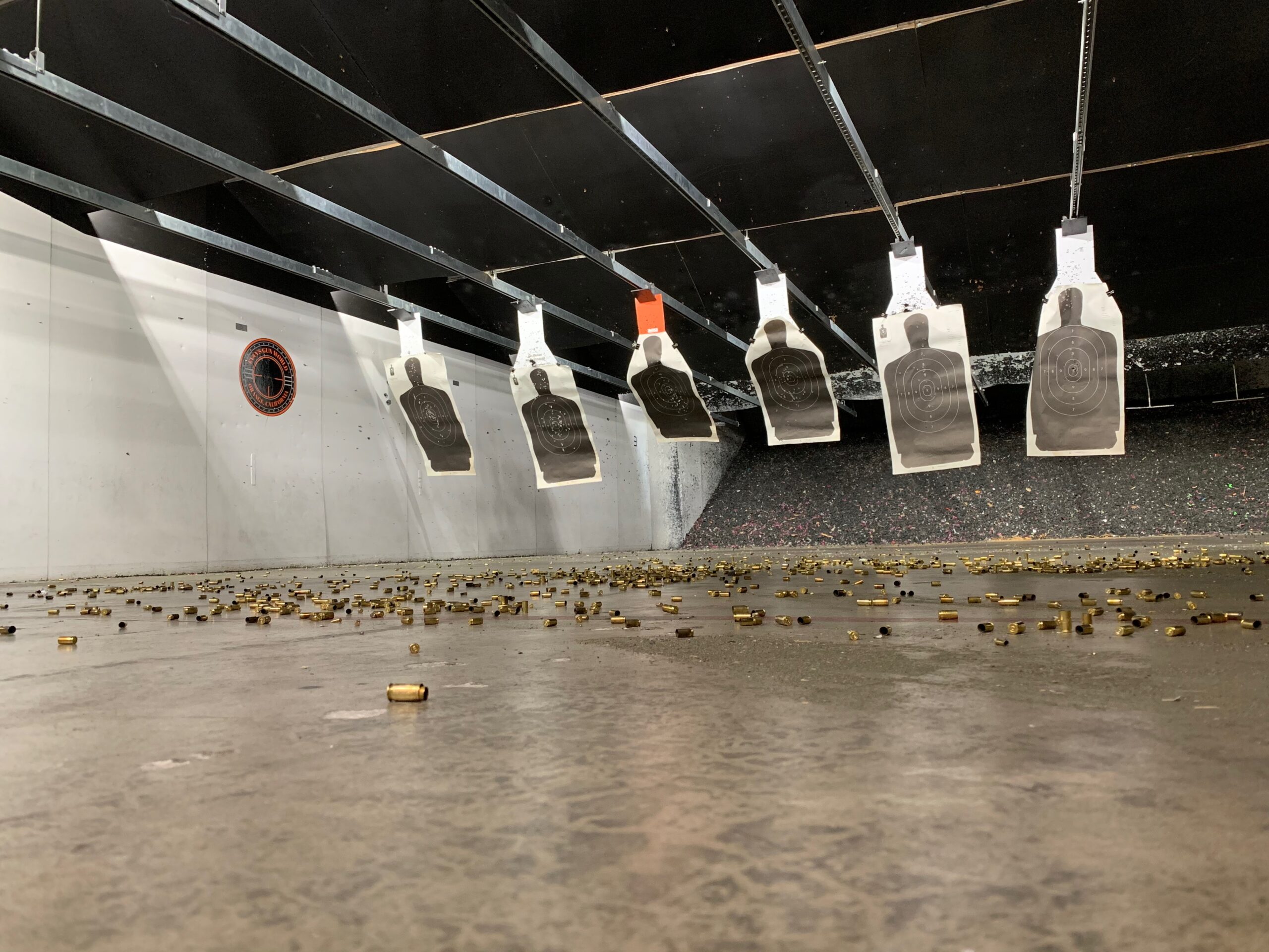 Six Black silhouette targets hanging downrange with casing on the floor of the gun range.